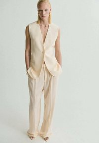 Chaleco beige a medida y pantalones de pierna ancha de tejido ligero, con cierre de un solo botón y bolsillos laterales. Textura suave y elegante.