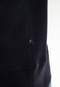Sudadera azul marino hecha de un tejido suave, con una etiqueta en la costura lateral y un dobladillo acanalado. La imagen de cerca muestra la textura y los detalles de la costura.