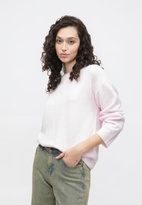 Roza pleten pulover z dolgimi rokavi in rebrastimi manšetami, združen s svetlo zelenimi jeans hlačami z rahlimi izpiranji. Preprost in sproščen dizajn.