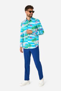 Kortärmad skjorta med knappar i ljusblått med ett tropiskt mönster av flamingor och palmer; kombinerad med blå byxor och vita sneakers.