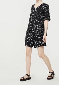 Svart topp och shorts-set med blommönster i vitt. Tyget är lätt och har en avslappnad passform. Matchat med svarta sandaler.