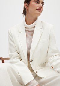 Valge bleiser ühe rinna_tasku, kahe eesnööbi ja vabalt langemisega, kombineeritud helebeezist ribakudumist turtleneckiga.
