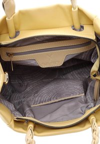 Żółta torebka z gładką skórzaną powierzchnią, plecionymi uchwytami oraz szarym materiałowym wnętrzem z kieszenią na zamek i wzorem tekstowym.