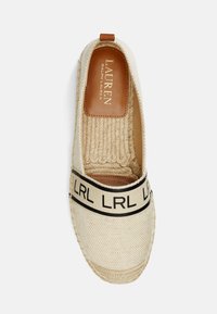 Zapato espadrille con una parte superior de lona beige tejida, tira de logo negra y suela de yute natural. Presenta un detalle de talón de cuero suave.
