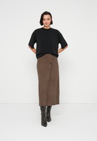 Μαύρο τοπ με κοντά μανίκια συνδυασμένο με μακριά καφέ φούστα από σουέντ με λεπτομέρεια κουμπιών στη μέση και μαύρες δερμάτινες μπότες μέχρι το γόνατο.