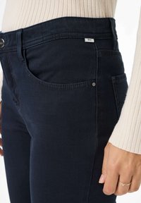 Dunkelblaue Jeans aus Denim mit Slim-Fit, ausgestattet mit Fronttaschen, sichtbaren Nähten und einem kleinen Markenetikett am Bund.