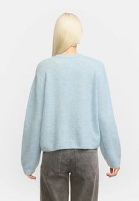 Ljusblå tröja med mjuk textur, med rund halsringning och neddragna axlar. Matchad med grå högmidjade jeans.