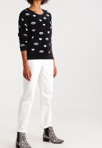 Black fluffy sweater with white lips and heart patterns, paired with white straight-leg jeans and animal print ankle boots.