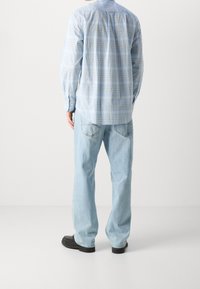 Camicia a quadri blu chiaro con colletto button-down, maniche lunghe e piega dietro, abbinata a jeans in denim a gamba larga di lavaggio chiaro e scarpe nere.
