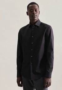 Schwarzes langärmliges Hemd aus glattem Stoff, mit durchgehendem Knopfleistenverschluss, spitzem Kragen und taillierter Passform, getragen zu dunkler Hose.