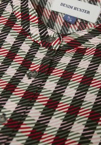 Chemise en coton multicolore avec un motif en losanges rouge, vert, noir et rose. Présente des boutons gris et un col rond. Étiquette visible.