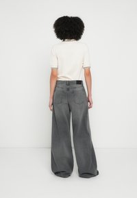 Széles szárú szürke farmernadrág elhalványult felülettel és látható varrással. Két hátsó zsebbel és fekete derékpánt cimkével rendelkezik.