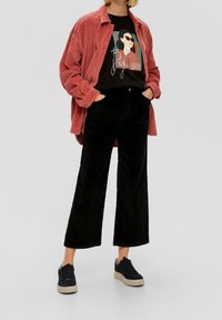 Červená kordurová overshirt nošená přes černé tričko s potiskem, doplněná černými širokými kordurovými kalhotami a černými teniskami.