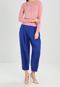 Ljusrosa långärmad cardigan med strukturerat mönster och knapplist, i kombination med löspassande blå byxor och nude högklackade skor.