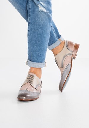 Des chaussures brogue de couleur claire avec un mélange de cuir lisse et perforé, présentant des tons gris, beige et rose, et un bout arrondi.