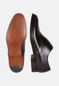Scarpe da uomo in pelle nera con tomaia liscia, dettagli con lacci, punta leggermente curva e suola in pelle marrone a contrasto con marchio impresso.