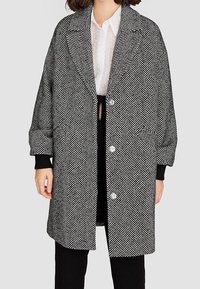 Haringbone-patroon jasje in zwart en wit, met een geknipt kraag, oversized pasvorm en twee voorzakken met knoopsluiting.