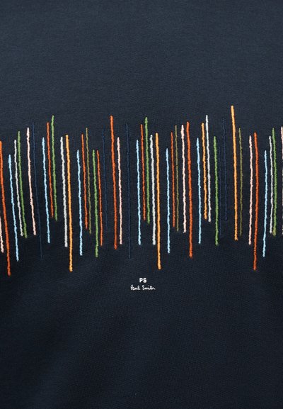 Πολύχρωμες κάθετες κεντημένες γραμμές διαφόρων μηκών σε σκοτεινό ύφασμα με μικρό λευκό κείμενο "PS Paul Smith" κάτω από το σχέδιο.