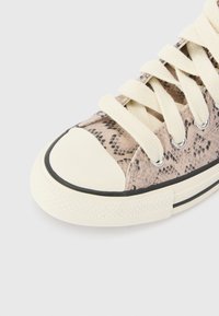 Sneaker med ett texturerat mönster i beige och svart orm, krämfärgade snören och en rundad vit gummitå med svart kant.