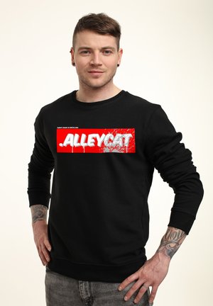 Černá mikina se výraznou červenou grafikou a bílým textem " .ALLEYCAT. " Design textu zahrnuje akcenty ve stylu rozstříknutí. Hladký povrch látky.