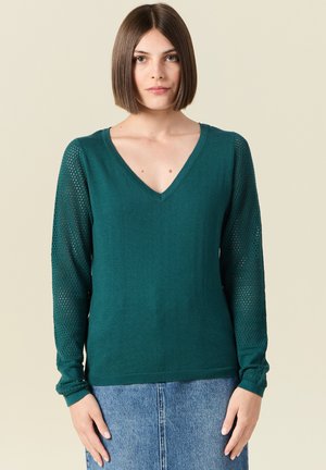 Teal gebreide trui met een V-hals en lange, gestructureerde mesh mouwen. Heeft ribben gebreide manchetten en zoom voor een aansluitende look.