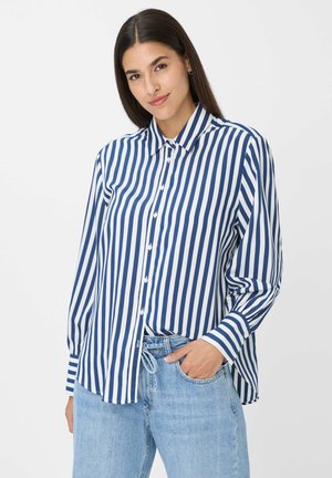 Overhemd met verticale blauw-witte strepen, kraag, lange mouwen en een relaxte pasvorm. Gepaarde met lichtblauwe jeans.