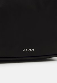 Surface texturé noir avec un petit logo de la marque "ALDO" en argent près du bord inférieur.