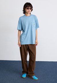 Lysblå stribet t-shirt med lomme, parret med brune løse bukser og blå sneakers med røde og orange striber. Klart design.
