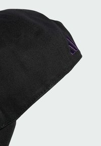 Gorra negra hecha de tela texturizada con un distintivo logo morado en el lateral. El diseño incluye una visera curvada y bordes cosidos.