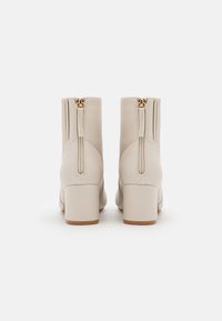Kremowe botki za kostkę o gładkiej skórzanej fakturze, z kwadratowym obcasem i podwójnymi złotymi zamkami z tyłu.