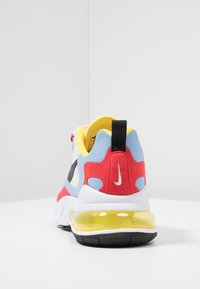 Vue arrière d'une chaussure Nike multicolore avec des accents rouges, bleus et jaunes, un onglet noir, une semelle blanche et une unité de coussin d'air jaune visible sous la semelle.