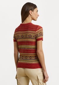 Pull en tricot rouge à manches courtes avec un motif à rayures dorées, noires et crème. Col et ourlet côtelés.
