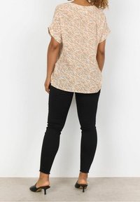 Top leggero a maniche corte color crema con motivo a onde arancioni. Abbinato a jeans neri aderenti e mule nere, che mostrano una vestibilità rilassata.