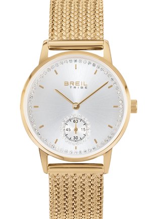 Guld-toneur med et struktureret mesh-bånd, rund sølvskive, fremhævet af en krystalramme og en sekundær sekundviser.