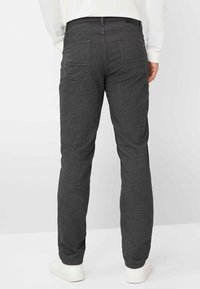 Donkergrijze broek van een gestructureerde stof, met een klassieke pasvorm, vijf zakken en subtiele rode stikselaccenten. Witte sneakers inbegrepen.