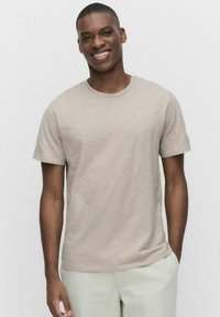 Beige kortærmet T-shirt lavet af et blødt, tekstureret stof, med rund hals og en afslappet pasform, båret med lyse bukser.