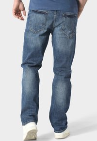 Vaqueros de mezclilla en azul medio con un acabado desgastado, diseño de pierna recta y dos bolsillos traseros. Zapatillas blancas con suelas texturizadas.