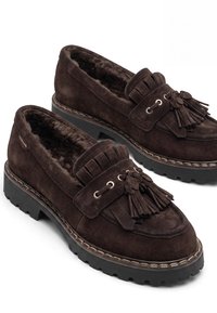 Σκούρα καφέ loafers από σουέντ με χοντρές μαύρες λαστιχένιες σόλες, λεπτομέρειες με φράτζες και φούντες και μαλακή, χνουδωτή εσωτερική επένδυση.