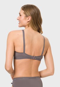 Gray bra with thin adjustable straps, soft texture, and a clasp closure at the back. Features logo detailing along the band.