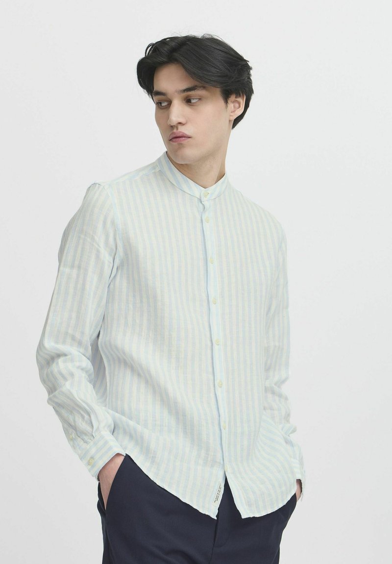 Camisa de manga larga a rayas azul claro con cuello alto y cierre de botón. La tela parece texturizada y ligera, con un ajuste casual.