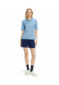 Polo shirt azzurro chiaro a maniche corte con colletto, abbinato a pantaloni corti blu navy. L'outfit è completato da sneakers bianche e calze nere.