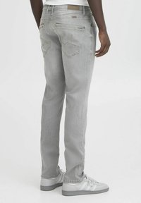 Jean de mezclilla gris claro con un corte ajustado, cinco bolsillos y detalles de costura sutiles. Combinados con zapatillas grises en un estilo casual.