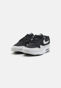 Baskets noires et grises avec des matériaux en mesh et en cuir, à bout rond, semelle intermédiaire blanche et semelle extérieure en caoutchouc noir. Présente le logo Nike sur les côtés.
