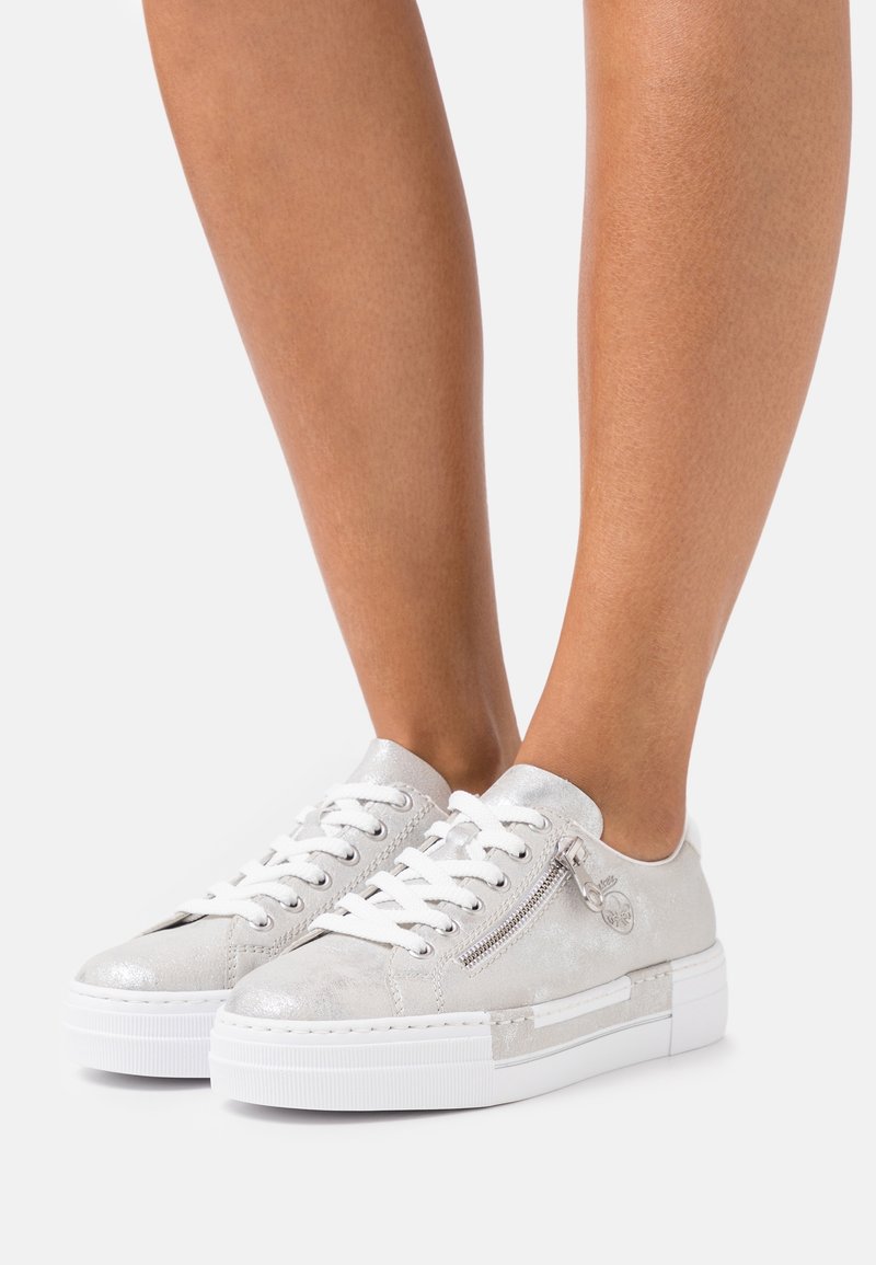 Sölj metallic sneakers med vita snören, som har en zip-detalj på sidan och en tjock vit sula, med en texturerad finish.