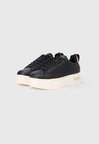 Black sneakers with a smooth leather upper, perforated design for breathability, thick cream-colored sole, and gold branding details.