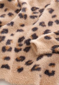 Mäkká, chlpatá látka s béžovým podkladom a tmavo hnedými, čiernymi a pieskovými leopardími škvrnami, zobrazujúca záhyby a detaily textúry.