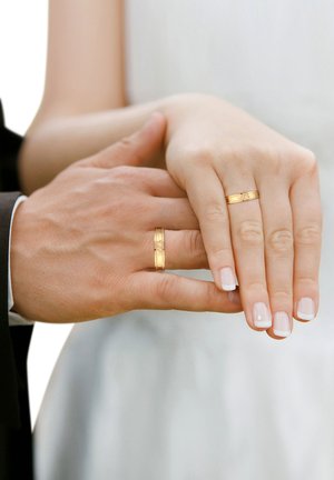 To hænder samlet, bærende guld vielsesringe. Den ene hånd har en enkel, glat ring, mens den anden har en mønstret guldring.