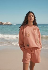 Set di felpa rosa e shorts realizzato in morbido tessuto, decorato con colorati ricami di motivi vegetali e testo.