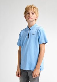 Ljusblå kortärmad polo skjorta i bomull, med en halvdragkedja och en liten svart logotyp på bröstet.