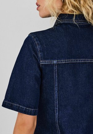 Tume teksariidest särg, millel on lühikesed varrukad, klassikaline krae, heledam õmblus ja tagaküljel yoke-detail.